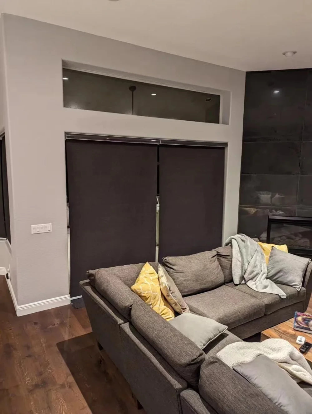 Decopedia motorized roller blinds installed on large living room window in blackout dark gray fabric, fully closed at night