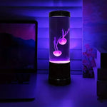 Color changing LED jellyfish night light glowing purple on desk next to monitor in dark room