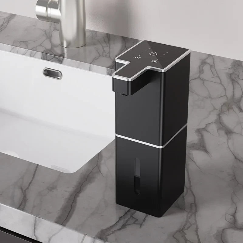 USB rechargeable automatic foam soap dispenser in black with silver trim on marble bathroom countertop next to sink