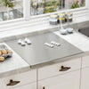 Large stainless steel cutting board on white marble kitchen countertop with garlic cloves and eggs nearby