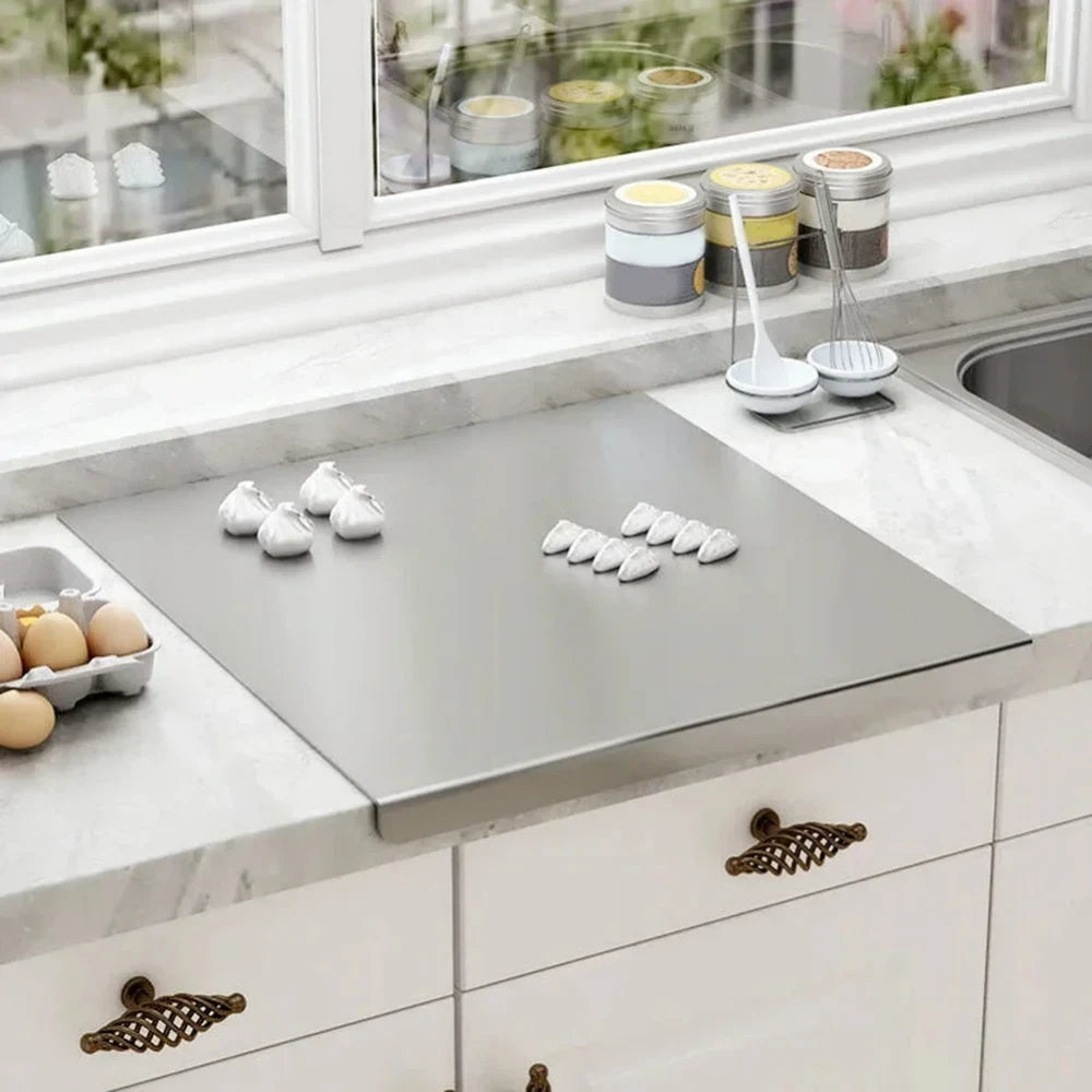 Large stainless steel cutting board on white marble kitchen countertop with garlic cloves and eggs nearby