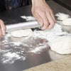Hands rolling dough on stainless steel kitchen cutting board with flour