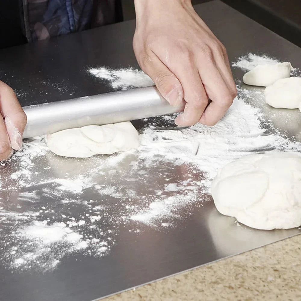 Hands rolling dough on stainless steel kitchen cutting board with flour