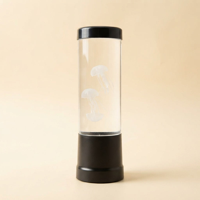 Color changing LED jellyfish night light with black base and clear cylindrical tank containing two white jellyfish, off, on beige background