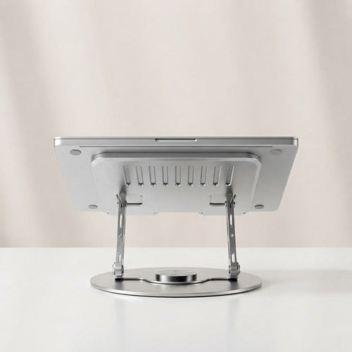 Silver metal laptop stand with 360-degree swivel round base and ventilated tray, rear view showing adjustable folding arms, on beige background