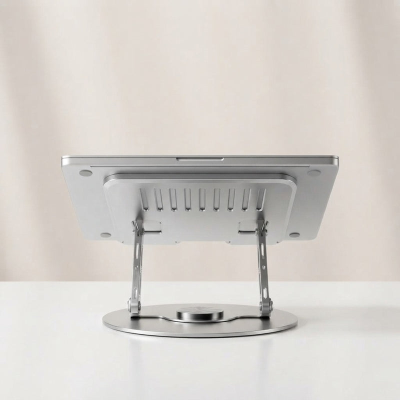 Silver metal laptop stand with 360-degree swivel round base and ventilated tray, rear view showing adjustable folding arms, on beige background
