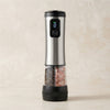 Rechargeable automatic salt and pepper grinder: single stainless steel unit with dual-chamber transparent base holding peppercorns and pink himalayan salt, LED display showing battery level, USB-C charging port, on beige background